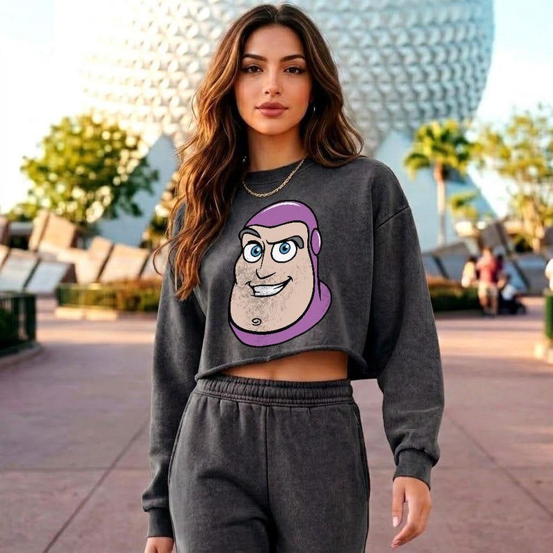 May include: A dark grey cropped sweatshirt featuring a graphic print of the character Buzz Lightyear's face with a purple hood, paired with matching dark grey sweatpants. The sweatshirt has long sleeves and a raw-cut hemline at the midriff.