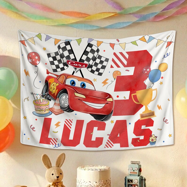 Puede incluir: Un tel&oacute;n de fondo rectangular de tela con un coche de carreras rojo, un n&uacute;mero 3 grande en rojo y el nombre LUCAS en letras rojas llamativas. El dise&ntilde;o incluye banderas a cuadros, un pastel, un trofeo dorado, globos y banderines.