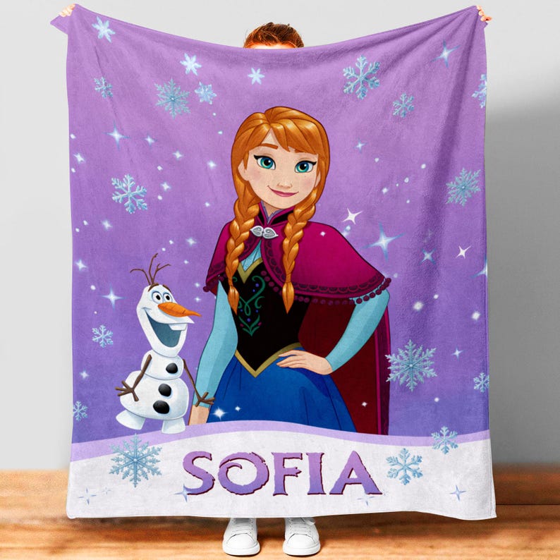 May include: A purple fleece blanket featuring a graphic of Anna from Frozen and Olaf the snowman. The background is decorated with light blue snowflakes and sparkles. The name SOFIA is printed in large purple letters on a white banner at the bottom.