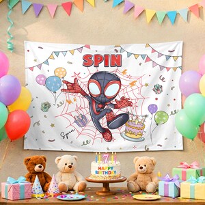 May include: A white rectangular birthday backdrop featuring a cartoon character in a black and red suit centered on a spider web. The text SPIN appears at the top. The design includes colorful bunting, balloons, gift boxes, and a birthday cake.