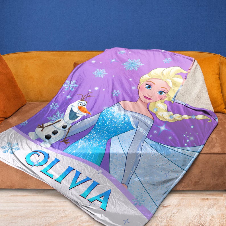 May include: A purple fleece blanket featuring a graphic print of a blonde character in a blue dress and a snowman character. The blanket is decorated with light blue snowflakes and includes the name OLIVIA printed in large blue letters at the bottom.