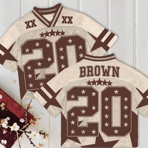 Pu&ograve; includere: Due maglie da football americano con un design a rete color crema e dettagli marroni. Le maglie presentano il numero 20, stelle e il nome "BROWN" sul retro. Le maniche hanno strisce marroni e il colletto &egrave; a V.