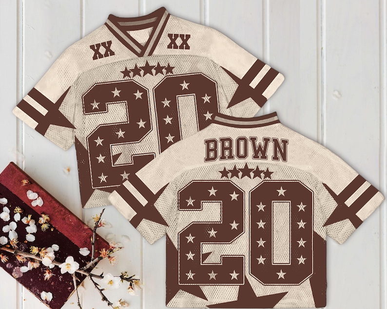 Pu&ograve; includere: Due maglie da football americano con un design a rete color crema e dettagli marroni. Le maglie presentano il numero 20, stelle e il nome "BROWN" sul retro. Le maniche hanno strisce marroni e il colletto &egrave; a V.