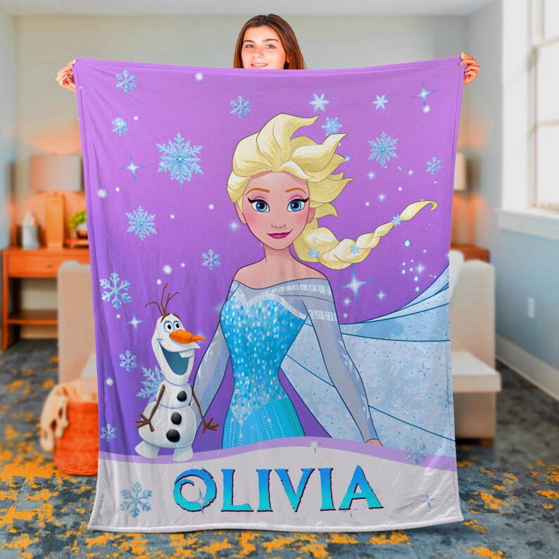 May include: A purple fleece blanket featuring a graphic print of Elsa with blonde hair and a blue dress, alongside Olaf the snowman. The design includes light blue snowflakes and stars, with the name OLIVIA printed in large blue letters at the bottom.