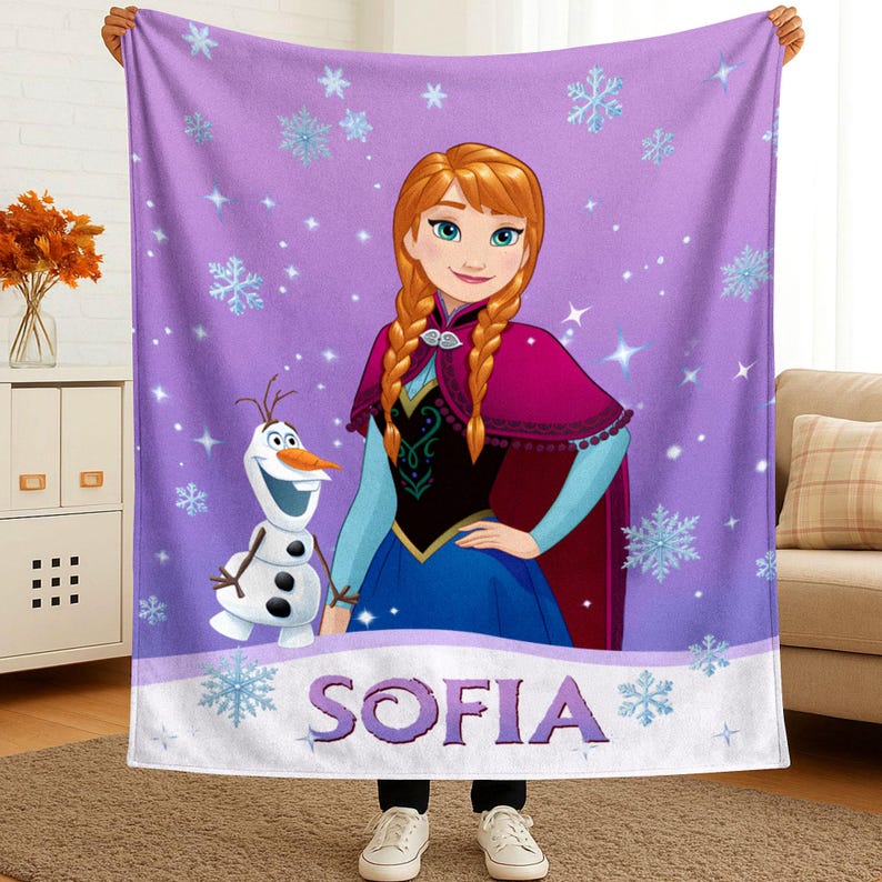 May include: A purple fleece blanket featuring a graphic print of Anna with braided hair and Olaf the snowman. The background is decorated with light blue snowflakes and sparkles. The name SOFIA is printed in large purple letters at the bottom.