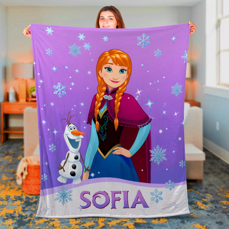 May include: A purple fleece blanket featuring a printed illustration of Anna from Frozen and Olaf the snowman. The design includes light blue snowflakes and stars scattered across the fabric. The name SOFIA is printed in large purple letters.