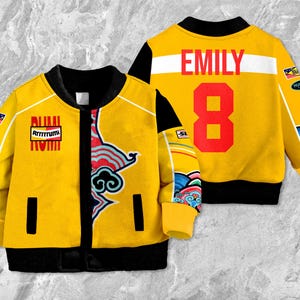 May include: A yellow bomber jacket with black trim, featuring the name "EMILY" and the number "8" on the back. The front has decorative patches and a colorful design. The jacket has a full-zip closure and ribbed cuffs.