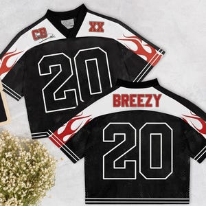 May include: Two black mesh jerseys with white and red flame designs. Each jersey has the number 20 in white, with "CB" and "XX" logos. One jersey has "BREEZY" across the back.
