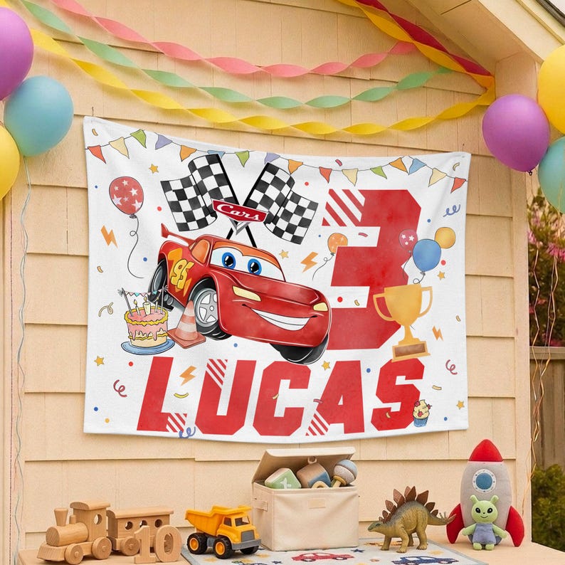 Puede incluir: Una pancarta rectangular de tela blanca con un coche de carreras rojo con el n&uacute;mero 95, dos banderas a cuadros, un trofeo dorado y un pastel de cumplea&ntilde;os. El n&uacute;mero 3 grande y el nombre LUCAS est&aacute;n impresos en letras rojas llamativas.
