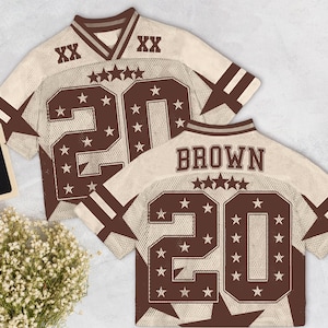 Pu&ograve; includere: Due maglie da football beige e marroni con il numero 20 e dettagli a stella. Una maglia ha il nome "BROWN" sul retro. Le maglie hanno un design a rete e strisce marroni sulle maniche.