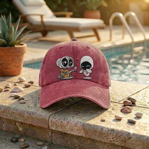 May include: A faded red baseball cap featuring an embroidered graphic of the robots WALL-E and EVE. The design shows WALL-E holding a small red heart toward EVE, who has a blue light on her chest. The cap has a structured crown and a curved brim.