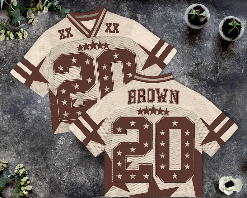 Pu&ograve; includere: Due maglie da football marroni e color crema. Ogni maglia ha il numero 20 in grandi lettere marroni con dettagli a stella. La parola "BROWN" &egrave; stampata sul retro di una maglia. Le maglie hanno strisce marroni sulle maniche.