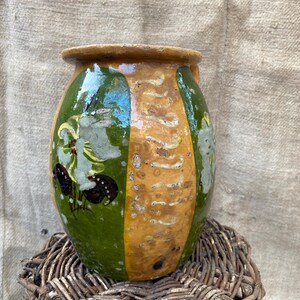 Può includere: Un vaso di ceramica vintage con un design dipinto in verde, giallo e bianco. Il vaso ha un corpo arrotondato e una bocca larga.