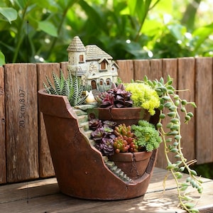 Peut inclure: Un pot en céramique marron décoratif avec une maison miniature et des marches, planté de diverses succulentes et plantes retombantes. Le pot mesure environ 20,5 cm de haut et présente un design rustique et vieilli.