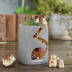 Peut inclure: Un pot de fleurs en béton gris avec un thème de hérisson fantaisiste. Le pot présente un design d'escalier avec des hérissons miniatures qui montent et descendent. Des figurines de hérissons supplémentaires sont placées autour du pot, créant une charmante scène de jardin.