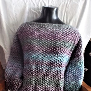 May include: A soft, knitted sweater with a loose fit and a wide neckline. The sweater is made in a multi-colored yarn with shades of purple, blue, and green.