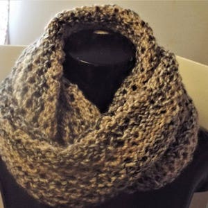 Könnte beinhalten: Ein brauner und grauer gestrickter Infinity-Schal. Der Schal ist aus einem weichen, strukturierten Garn gefertigt und perfekt, um sich im Winter warm zu halten.
