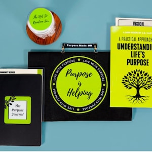 May include: An overhead shot of stationery items, including a black spiral-bound journal with "The Purpose Journal" text, a mini-book titled "A Practical Approach to Understanding Life's Purpose", and a black banner with "Purpose is Helping" text. A wooden jar is also visible.