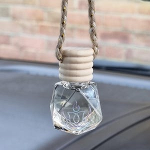 May include: Clear, faceted glass car air freshener with a light-coloured wooden cap and a decorative design. The air freshener hangs from a braided cord with gold accents, offering a subtle, stylish aesthetic for vehicle interiors.