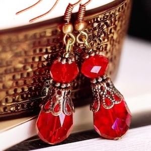 May include: Red glass teardrop earrings with ornate gold-toned metal accents. The earrings have a vintage style.