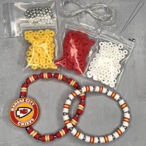 May include: A bracelet-making kit featuring red, yellow, and white beads, along with silver-colored spacers. The kit includes two bracelets, one with a Kansas City Chiefs logo charm. The beads are in small plastic bags.