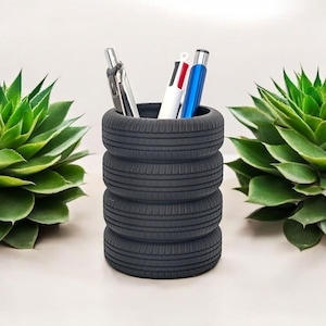 May include: A desk tidy made from four stacked black tyre treads, holding pens. Two green succulent plants are on either side. The design is a creative way to repurpose materials.