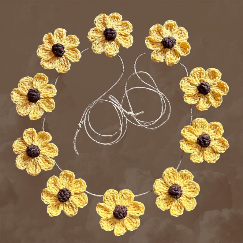 May include: A garland of crocheted yellow sunflowers with brown centers, strung together with twine. The garland is laid out in a circle on a brown background.