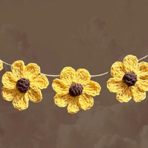 May include: A garland of crocheted yellow sunflowers with brown centers. The sunflowers are strung together with twine.