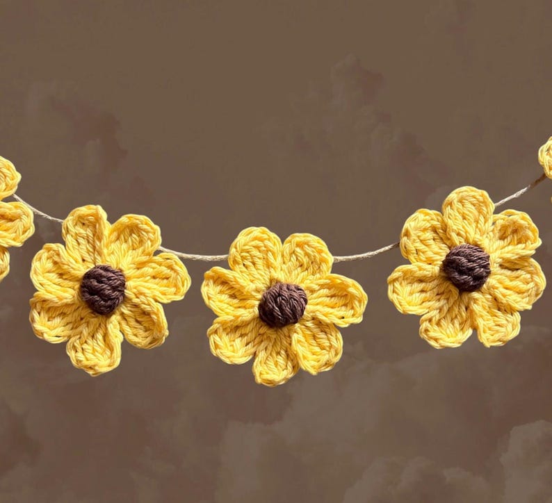May include: A garland of crocheted yellow sunflowers with brown centers. The sunflowers are strung together with twine.