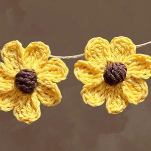 May include: Two crocheted yellow sunflower decorations with brown centers, strung on a white twine.