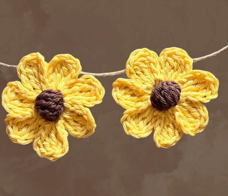 May include: Two crocheted yellow sunflower decorations with brown centers, strung on a white twine.