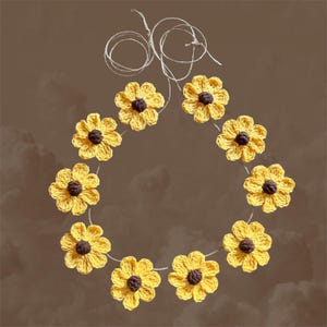 May include: A garland of crocheted yellow sunflowers with brown centers, strung together with twine.