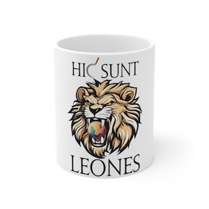 May include: White ceramic mug with a lion's head illustration. The lion is biting a colorful ball with the text "Hic Sunt Leones" printed above and below the image.