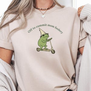 May include: A white ceramic mug with a black handle and the text "But First, Coffee" in a bold, black font. The mug is set against a blurred background, suggesting a cozy setting. The mug appears to be approximately 4 inches tall.