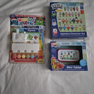 May include: An assortment of Numberblocks educational toys, including a paint-and-play train set, an alphabet character set, and a mini tablet. The packaging features colorful graphics and text promoting learning through play for children aged 3 and up.