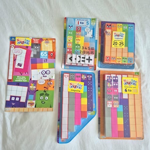 May include: A collection of Numberblocks educational items including a magazine and four sets of buildable block figures in colourful packaging. The sets feature various numbered characters, mathematical symbols, and stickers with bright, multi-coloured designs.