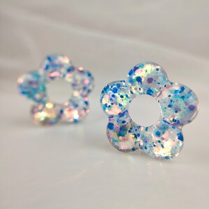 May include: A pair of iridescent blue and white flower-shaped earrings with glitter embedded in the resin.