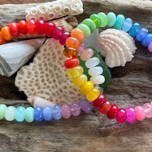 Puede incluir: Dos pulseras de cuentas de colores arcoíris con una variedad de colores que incluyen rojo, naranja, amarillo, verde, azul, morado y rosa.