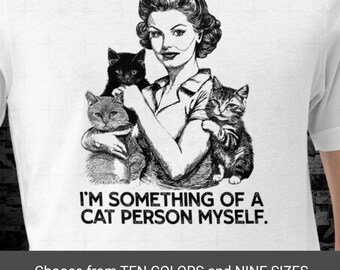 May include: White t-shirt featuring a vintage-style illustration of a woman holding three cats. The text "I'M SOMETHING OF A CAT PERSON MYSELF" is printed below the image. The bottom of the image includes the text "Choose from TEN COLORS and NINE SIZES."