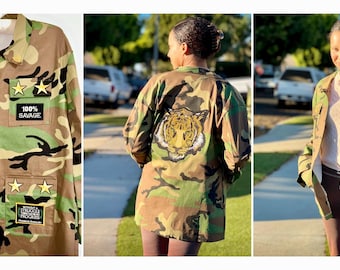 May include: Camouflage print jacket with multiple patches and star accents. The jacket features text patches that read "DON'T MISTAKE MY KINDNESS FOR WEAKNESS", "100% SAVAGE", and "BLACK". A tiger graphic is on the back.