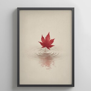May include: Framed art print featuring a vibrant red maple leaf floating on water, creating concentric ripples. The leaf's reflection is visible below. The background is a soft beige, and the frame is black.