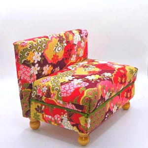 May include: A small, upholstered armchair with a vibrant floral pattern in red, yellow, pink, and white. The chair has a straight back, a cushioned seat, and four wooden legs. The trim is green.