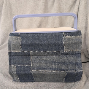 May include: A light blue speaker with a denim patchwork cover and a handle. The speaker is sitting on a light gray surface.