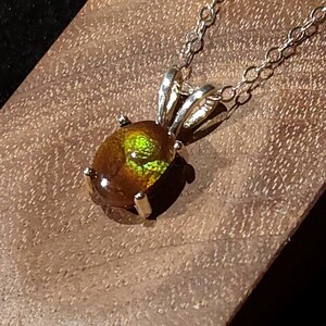 May include: A pendant necklace featuring an oval-shaped, iridescent ammolite gemstone with vibrant green and orange flashes, set in a silver-toned metal prong setting and suspended from a delicate silver-toned chain link necklace.