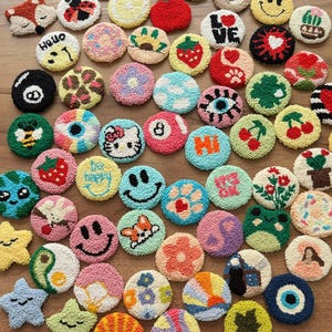 May include: A collection of colorful, round, hand-stitched felt ornaments with various designs, including smiley faces, flowers, animals, and words like "Hi" and "Be Happy".