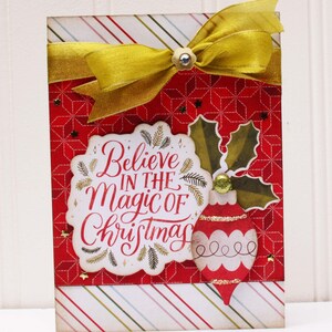 May include: A red and white Christmas card with a gold ribbon and a gold ornament. The card says "Believe in the Magic of Christmas".
