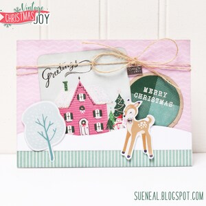 May include: A pink and white Christmas card with a house, a deer, a tree, and the words "Greetings" and "Merry Christmas".