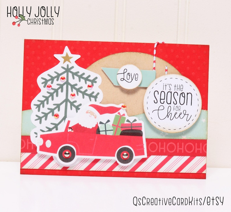 May include: A red Christmas card with a white Santa Claus driving a red car with a Christmas tree in the back. The card has a red and white striped border and the text "It's the season for cheer" and "Love" on it.