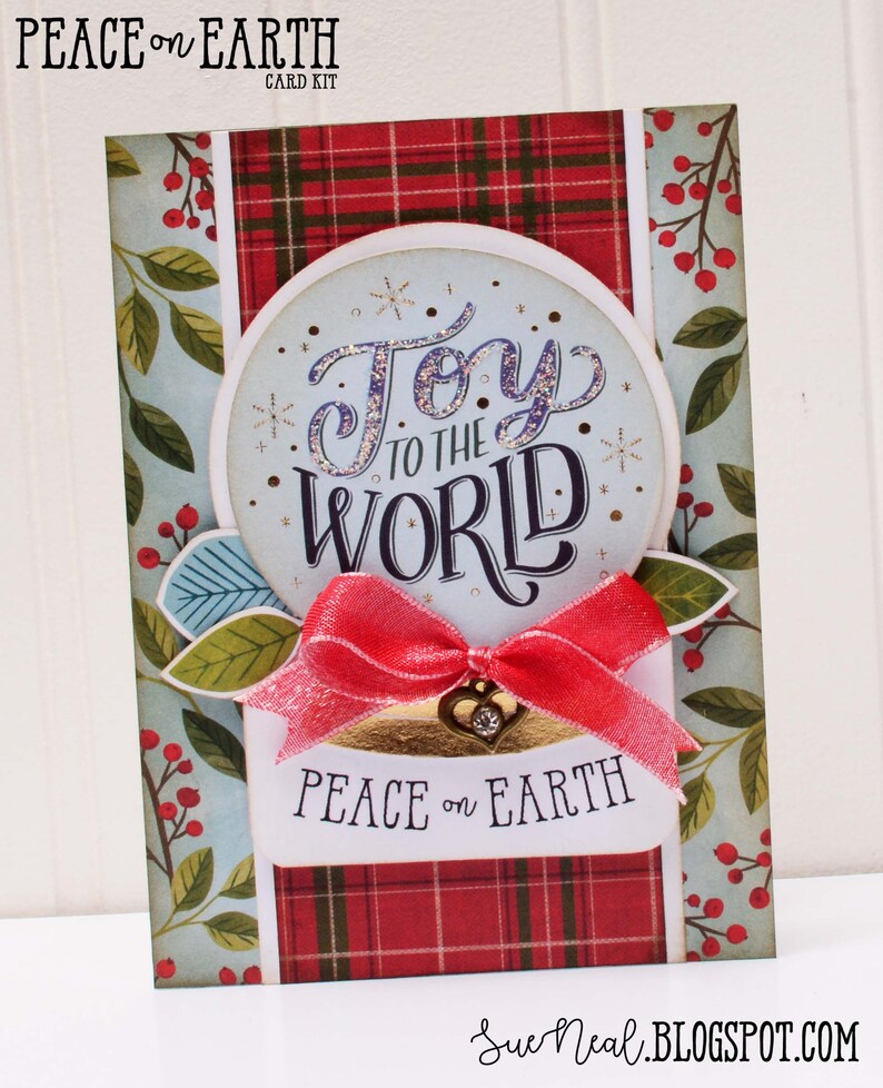 May include: A Christmas card with a red and green plaid background and a blue circle with the text "Joy to the World" in sparkly purple letters. The card also has a red ribbon and the text "Peace on Earth" in black letters.