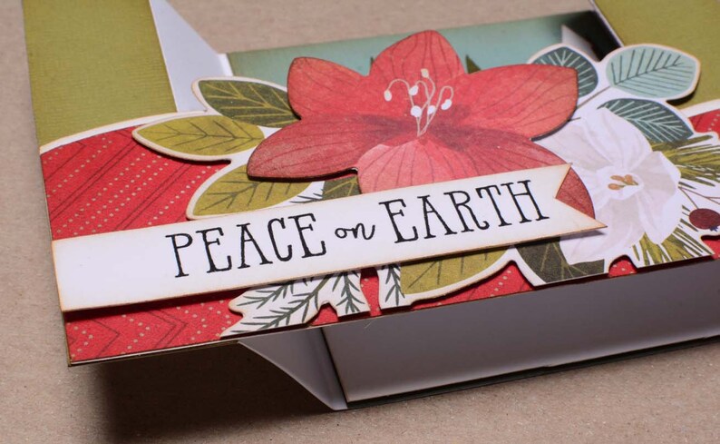May include: A handmade card with a red, white, and green floral design. The card has a banner that says "Peace on Earth".